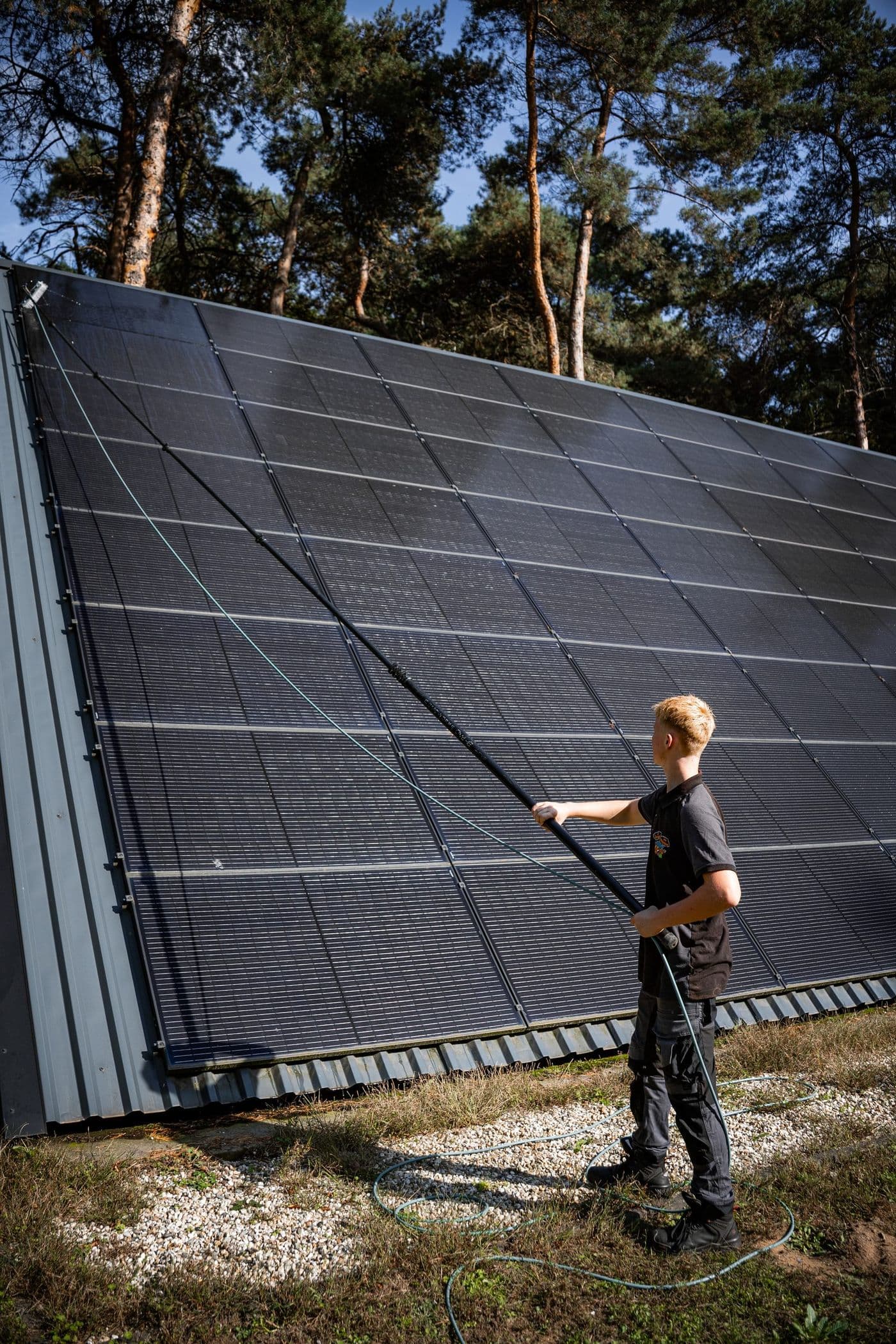Medewerker reinigt zonnepanelen met een telescoopborstel