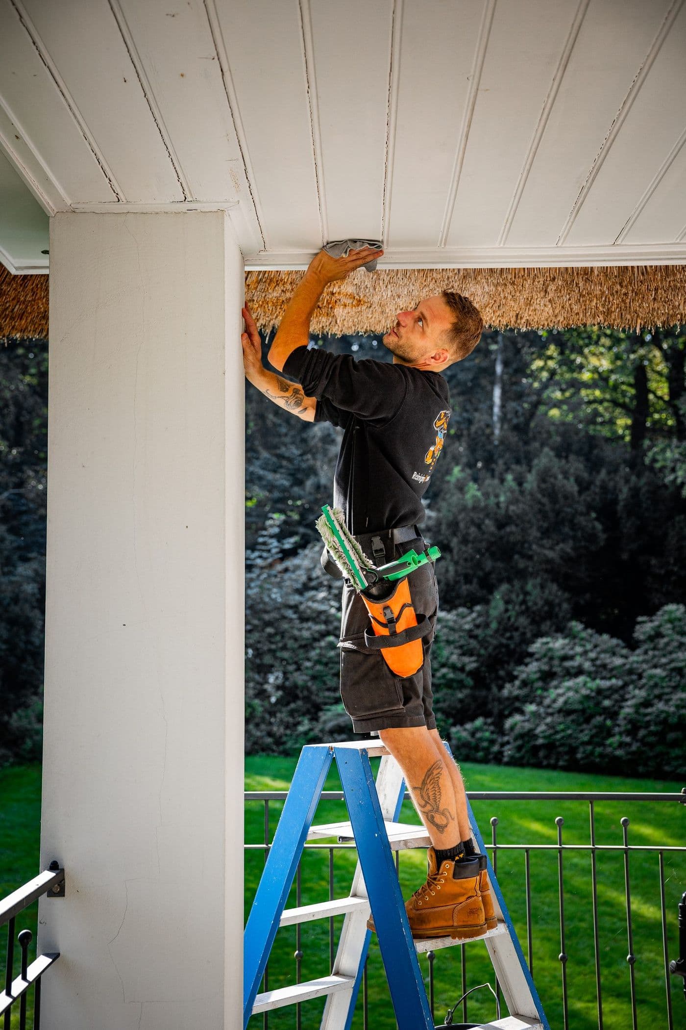Medewerker op een trap reinigt het houtwerk van een veranda