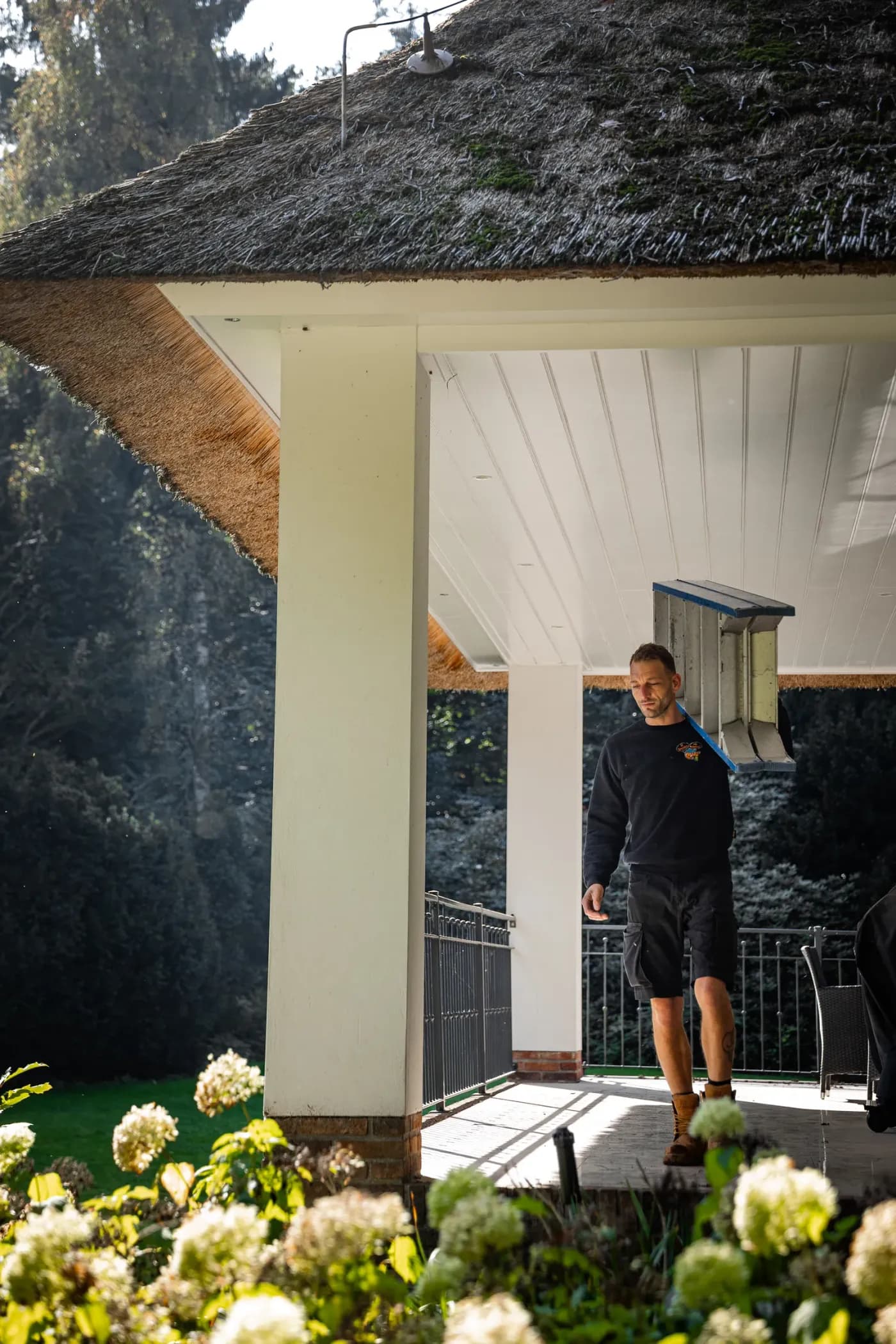 Medewerker van Specialist van Nederland draagt een ladder over de veranda van een woning