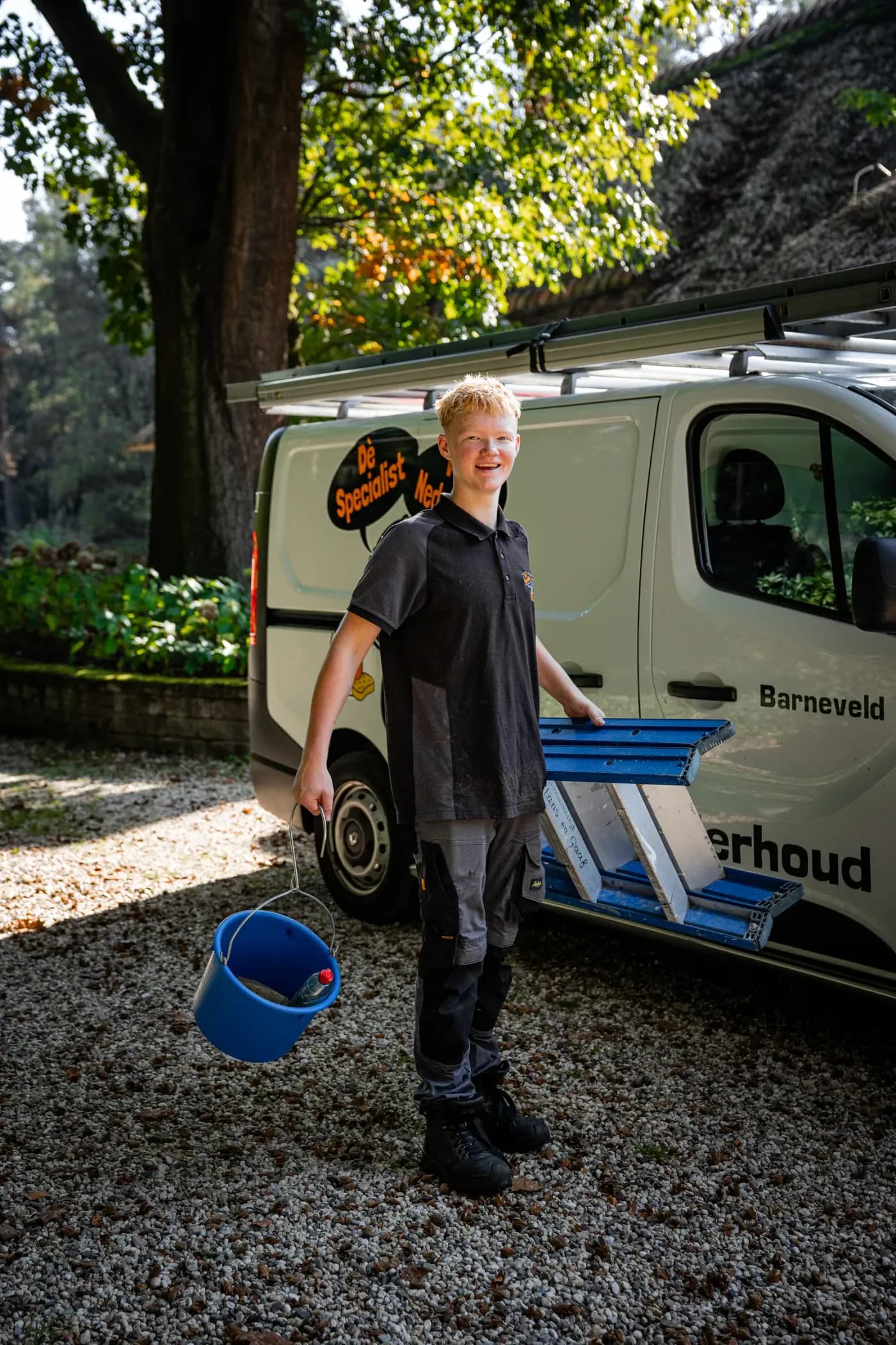 Lachende medewerker met emmer en ladder bij de bus van Specialist van Nederland